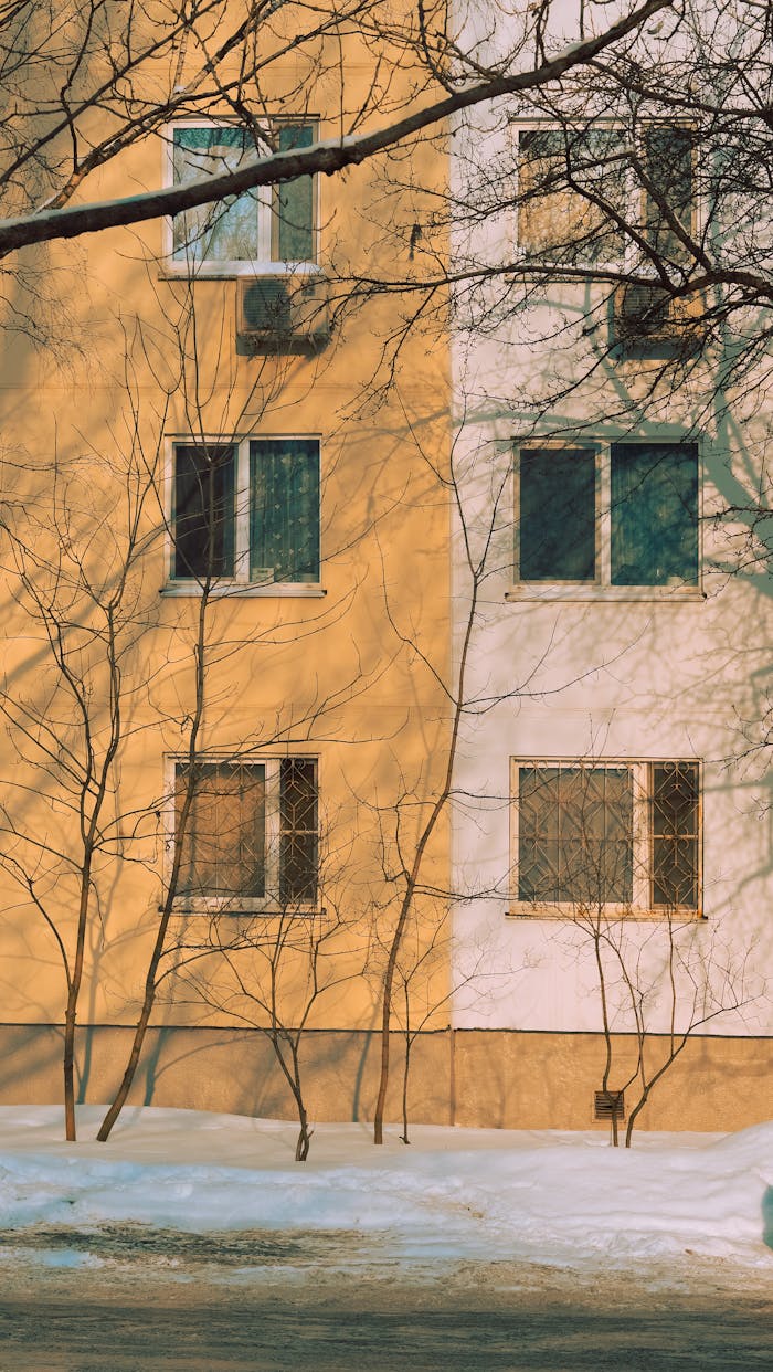 Apartment building facade with shadow play in winter setting, capturing sunlight and snow.