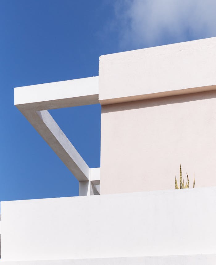 A modern minimalist building with white plaster walls against a bright blue sky, showcasing geometric design.